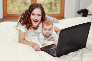 Smiling young mom holding a baby while working with a laptop