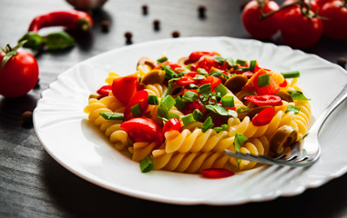 fusilli pasta salad with tomato and olive in plate on dark wooden background