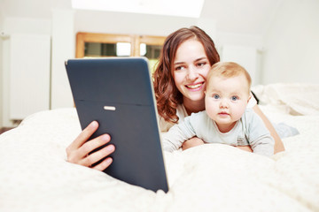 Woman reading e-book with baby on bed