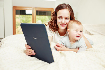 Woman reading e-book while lying on bed with baby