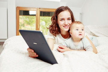 Woman holding e-book while layig on bed with baby