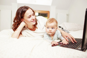 Woman using laptop while laying on bed with baby