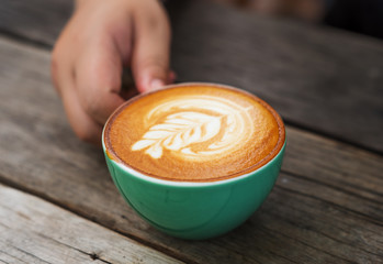 Hand womeen with cappuccino coffee in a green cup on wooden