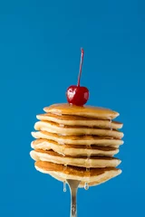 Rolgordijnen Stack of pancakes with honey decorated sweet cherry pinned on a fork on blue background © thayra83
