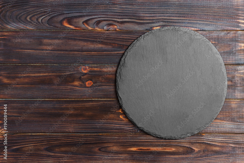 Poster Round natural slate board. Dark gray slate stand on wooden background. Natural restaurant utensil