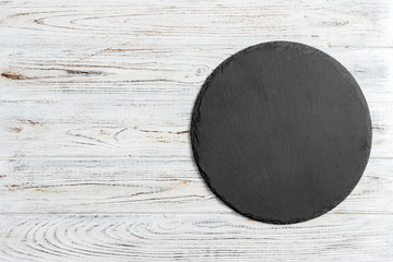 Black slate round stone on wooden background, top view, copy space