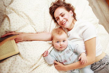 Smiling young woman with book and baby on a bed