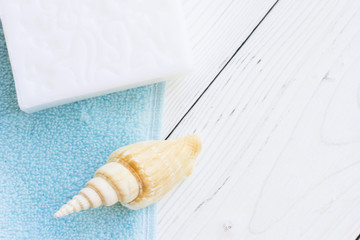 Natural Sea Spa Elements on white wooden background.White and blue clean towels, hand made natural soap and sea shells, top view, flat lay, copy space