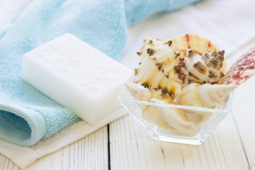 Natural Sea Spa Elements on white wooden background.White and blue clean towels, hand made natural soap and sea shells in a glass bowl