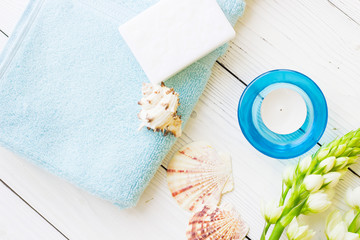Aromatherapy Spa Concept mock up with a fragrant candle in a blue candle holder, a bar of soap, terry towels, sea shells and white flower on white wooden background, top view