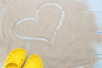yellow flip flops and heart on white beach sand.