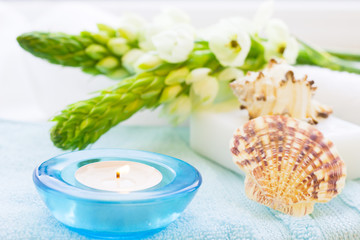 Aromatherapy Spa Concept with a fragrant candle in a blue candle holder, a bar of soap, terry towels, sea shells and white flower on white wooden background, selective focus