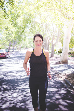 Beautiful brunette female fitness model running / stretching / exercising outside in a leafy and green suburb