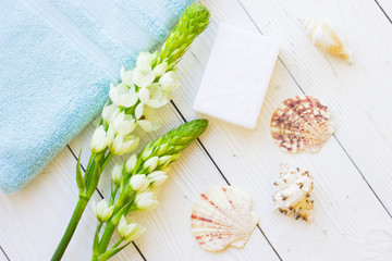 Aromatherapy Spa Concept mock up with a bar of soap, terry towels, sea shells and white flower on white wooden background