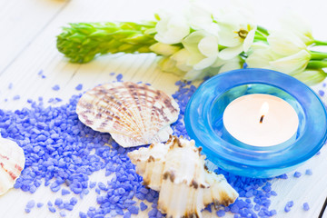 Spa Treatment Concept with natural lavender bath salt, an aroma candle in a blue candle holder, fresh white flowers and sea shells on a white wooden table, top view