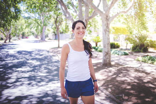 Beautiful brunette female fitness model running / stretching / exercising outside in a leafy and green suburb