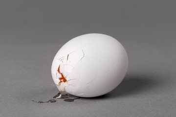 Broken white egg with a crack through which you can see the yolk. Gray background