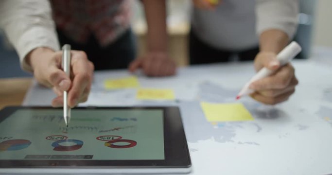 4K Close up on hands of unrecognizable business team in a meeting, brainstorming with world map & checking financial data on tablet. Slow motion.