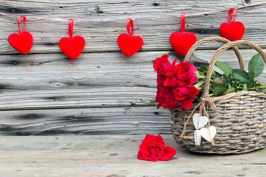 Rote Rosen im Weidenkorb mit Herzen rustikal vor Holzhintergrund