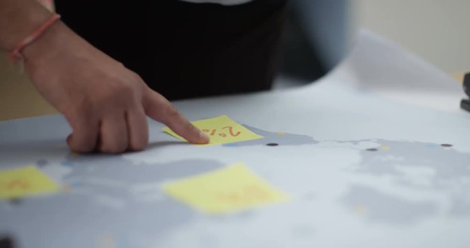 4K Close up hands of business team in a meeting, putting sticky notes on world map. Slow motion.