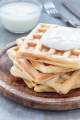 Homemade savory belgian waffles with bacon and shredded cheese, served with plain yogurt, on wooden plate, vertical