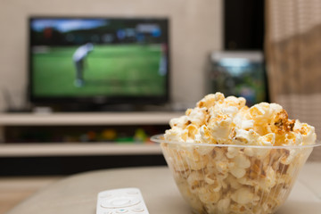 popcorn and remote control on sofa with a TV broadcasting golf match on background