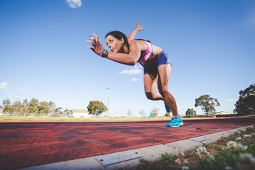 Fototapeta na wymiar Female fitness model and track athlete sprinting on an athletics track made from tartan