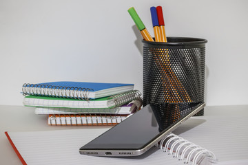 Open notebook with a mobile phone on it with colored notepads and a glass with multi-colored pens as background Office supplies - Powered by Adobe