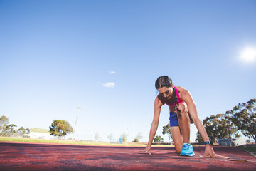Female fitness model and track athlete sprinting on an athletics track made from tartan