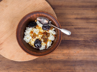 Curd in an earthenware bowl with the raisins, and dried apricots drizzled with honey on background of the table and cutting board. Healthy meals Illustration for blog articles or advertising.