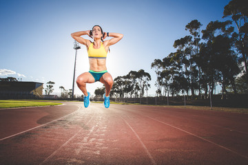 Female fitness model and track athlete sprinting on an athletics track made from tartan