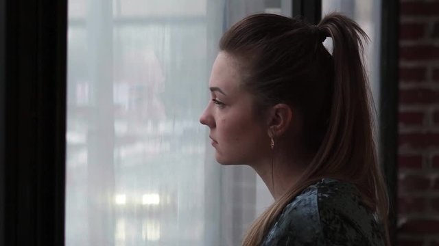 Close-up of a young sad woman looking out the window