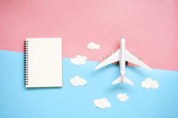 Flat lay design of travel concept with plane, blank notebook and cloud on blue and pink background...