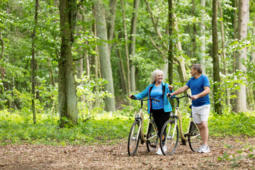 Naklejka premium Older marriage standing with bicycles in the forest.