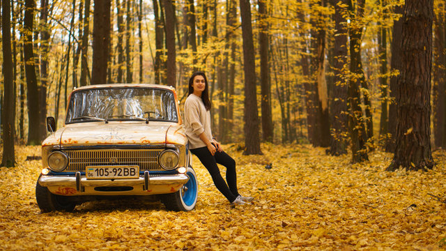 Young brunette girl stands near a retro car in an autumn forest
