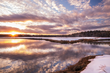 Beautiful winter sunset on the river bank. Forest in the frost in the distance. USA. Maine.
