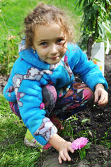 curly girl with a happy expression on his face working in the garden in the spring, removes leaves, debris, branches after the winter, planting flowers and seedlings.