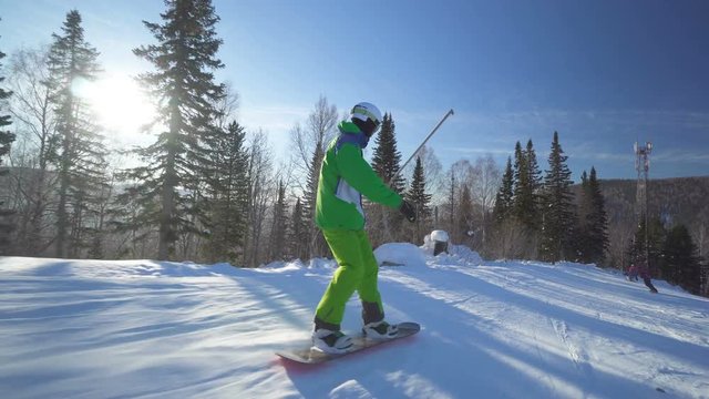 Sportsman on board in bright green clothes rides down fastly upon a slope of the hill at sunny winter day