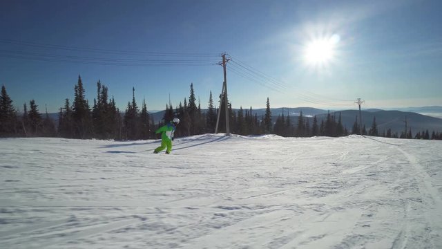 Sportsman on board in bright green clothes rides down upon a slope of the hill at sunny winter day
