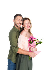 smiling man hugging wife with bouquet of flowers and postcard isolated on white