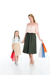 stylish mother and daughter with shopping bags holding hands isolated on white