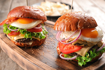 Tasty burgers with fried eggs on wooden tray, closeup