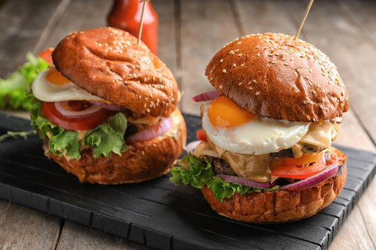 Tasty burgers with fried eggs on table