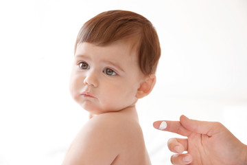 Woman applying body cream on her baby against light background