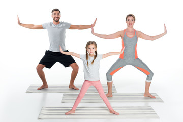 Obraz premium athletic family practicing yoga on mats together isolated on white