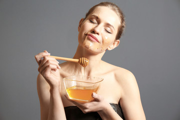 Young woman applying honey on her face against grey background. Skin treatment