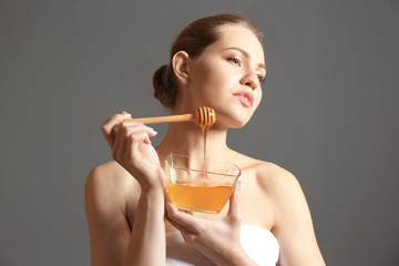 Young woman with bowl of honey on grey background