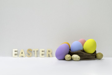 The decorated colorful easter eggs in the brown jute bag with white background and wooden easter alphabets