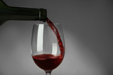 Pouring red wine into glass on gray background