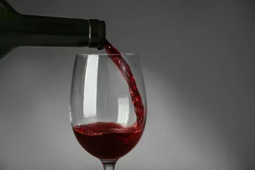 Fotobehang Pouring red wine into glass on gray background © Africa Studio